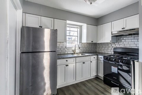 A kitchen with a stainless steel refrigerator, black stove, and white cabinets.