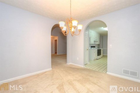 A spacious room with a chandelier and a view of a kitchen through an archway.
