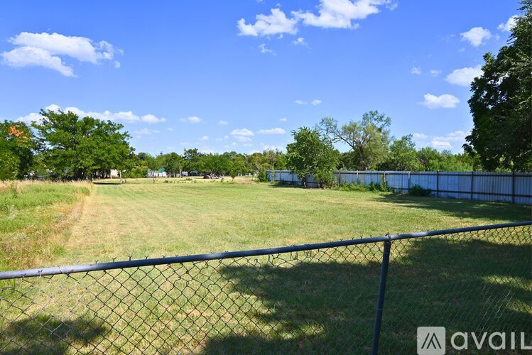 A fenced field with trees in the distance under a blue sky.
