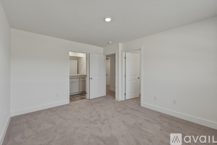 A spacious room with carpeted floor and white walls, with a door on the right and a window on the left.