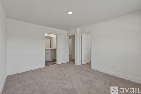 A spacious room with carpeted floor and white walls, with a door on the right and a window on the left.