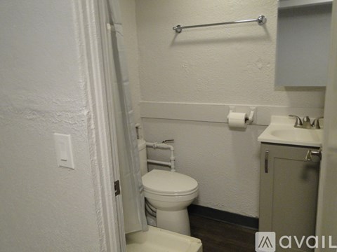 A white toilet in a small bathroom with a white sink and a towel bar.