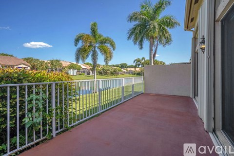 A balcony with a red floor and a metal railing with a view of palm trees and a blue sky.