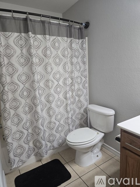 A bathroom with a toilet, a shower curtain and a mat.