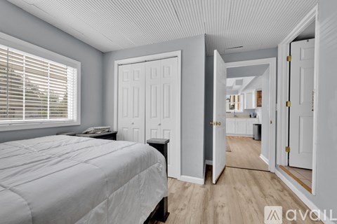 A bedroom with a bed, a window with blinds, and a door leading to another room.