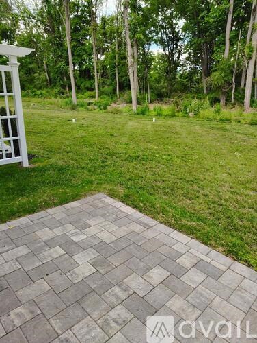 A patio with a white pergola and a grassy area with trees in the background.