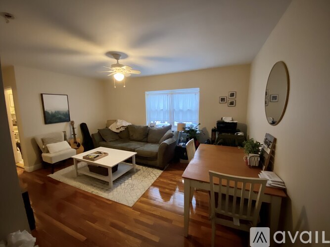 A living room with a couch, a coffee table, a chair, a ceiling fan, and a window.