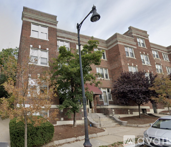 A street view of a residential area with a large red brick building, a tree, and a lamp post.