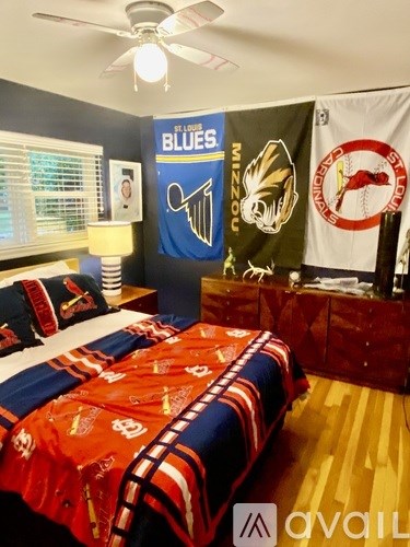 A bedroom with a bed covered in a red and blue comforter and a ceiling fan.