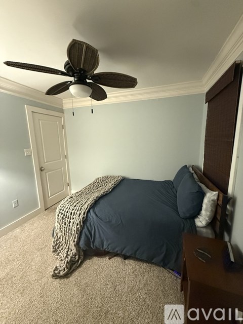 A bedroom with a bed covered in a blue blanket and a ceiling fan.