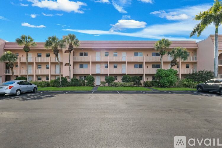 A parking lot in front of a pink building with palm trees.