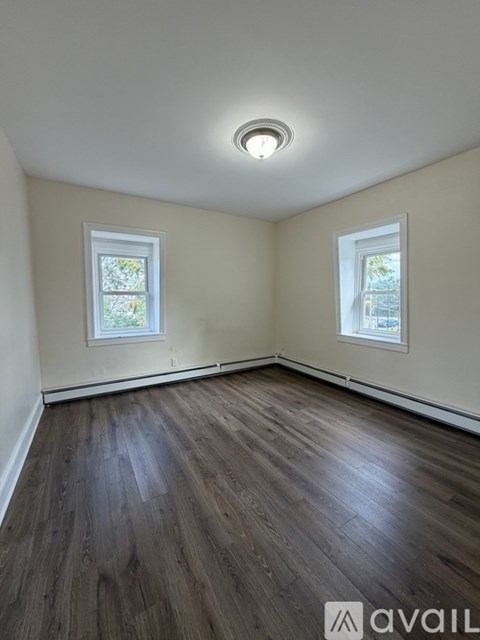 A room with wooden flooring and two windows.