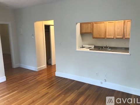 A room with wooden floors and a kitchenette with wooden cabinets.