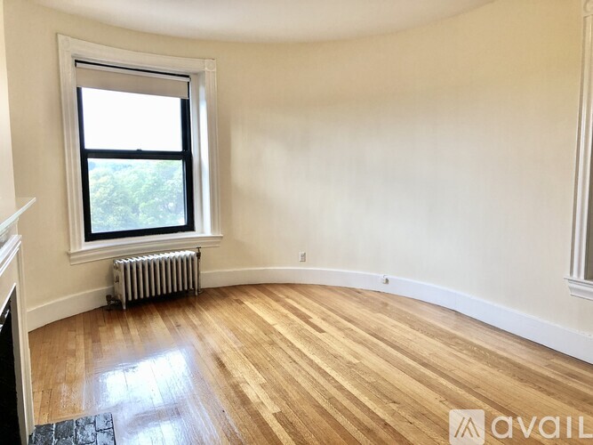 A room with wooden flooring and a window with a radiator beneath it.
