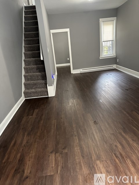 A room with wooden flooring and a staircase with a carpeted runner.