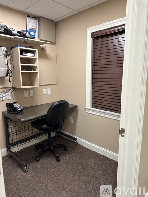 A small office with a black chair and a desk with a phone on it.