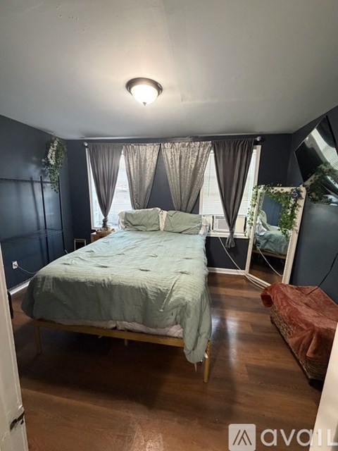 A bedroom with a bed, a window with curtains, and a wooden floor.