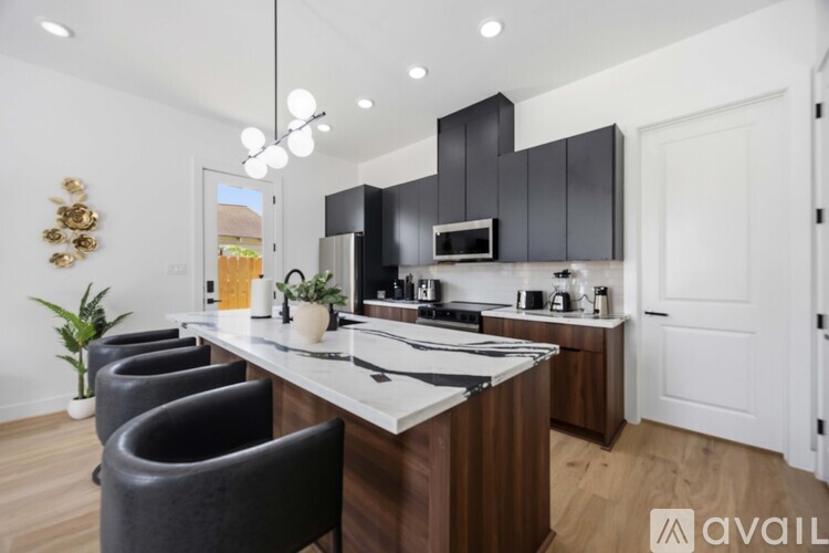 A modern kitchen with a long island and black chairs.