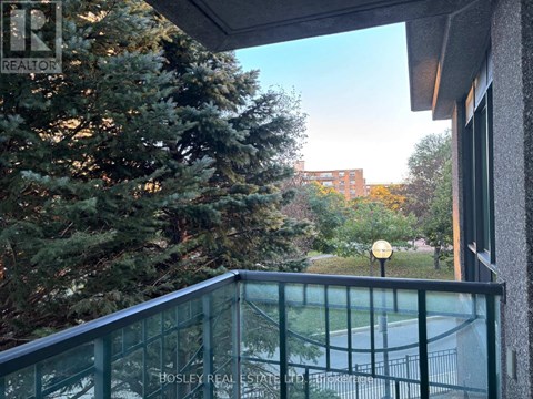 A balcony with a glass railing and a view of a tree and a building.