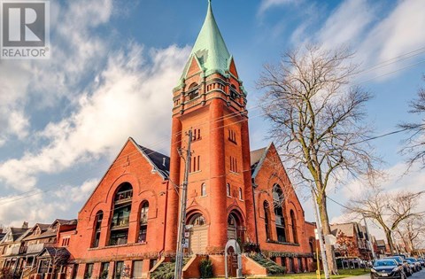 A church with a green steeple stands in front of a row of houses.