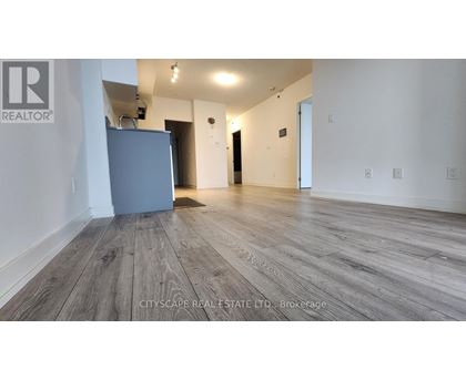 A spacious room with wooden flooring and a grey refrigerator.