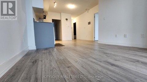 A spacious room with wooden flooring and a grey refrigerator.