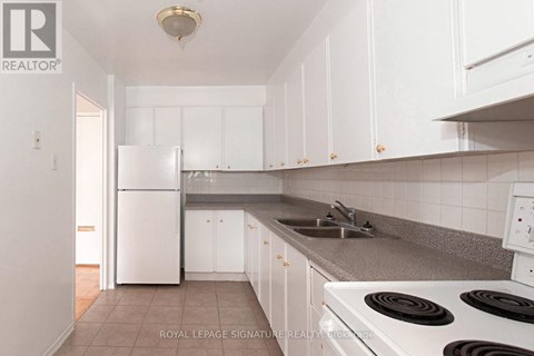 A white kitchen with a refrigerator, sink, and stove.