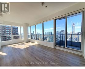 A spacious room with wooden floors and large windows overlooking a cityscape.