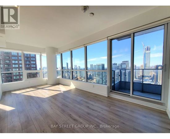 A spacious room with wooden floors and large windows overlooking a cityscape.