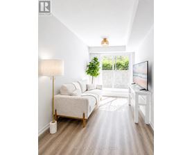 A well-lit, minimalist bedroom with a large bed, a small table, and a television.