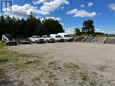 A gravel lot with a row of parked cars and a trailer.