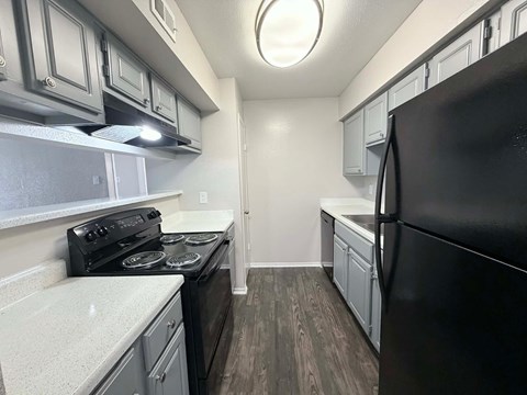 A black refrigerator is in the corner of a kitchen with white cabinets.