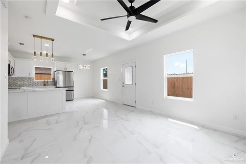 A spacious, empty room with white marble flooring and a ceiling fan.