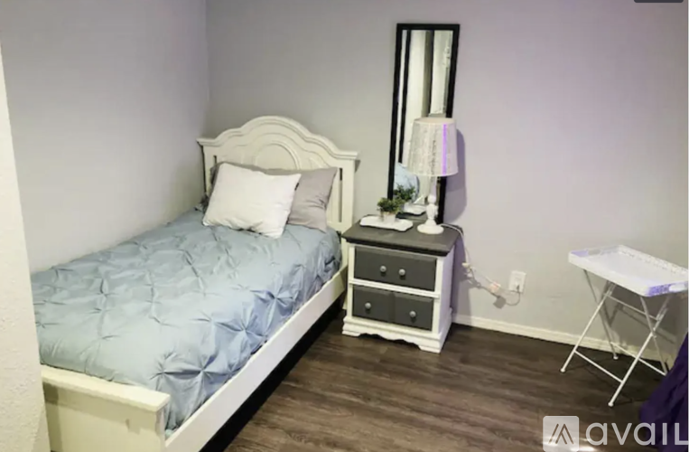 A bedroom with a bed, nightstand, lamp, and ironing board.