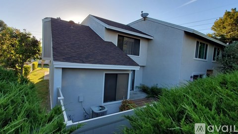 A house with a grey roof and a white wall is surrounded by greenery.