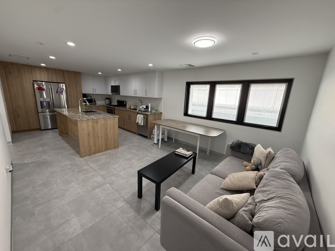 A modern living room with a grey sofa and a kitchen area in the background.