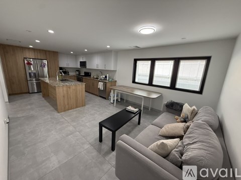 A modern living room with a grey sofa and a kitchen area in the background.