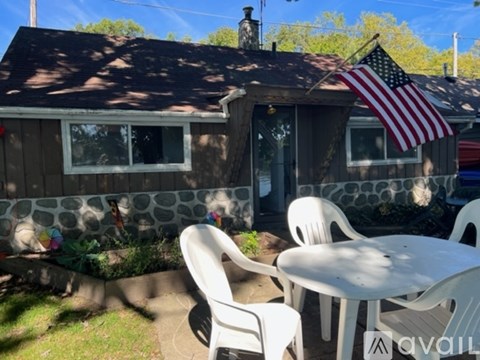 A small house with a flag on the roof and a white table and chairs in front.
