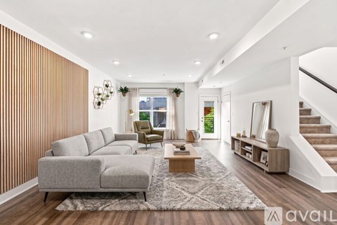 A spacious living room with a grey sofa, wooden flooring, and a staircase on the right.
