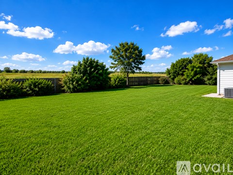 A large, well-maintained lawn with a white shed and a few trees in the distance under a blue sky with scattered clouds.