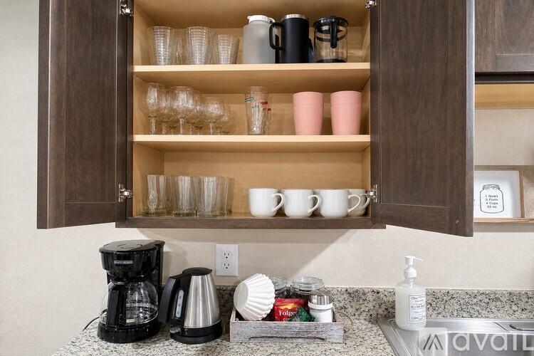 A kitchen cabinet with coffee cups and glasses on the shelf.
