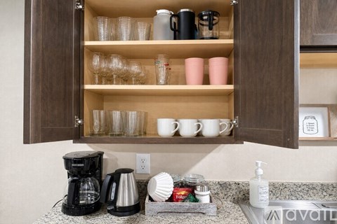 A kitchen cabinet with coffee cups and glasses on the shelf.