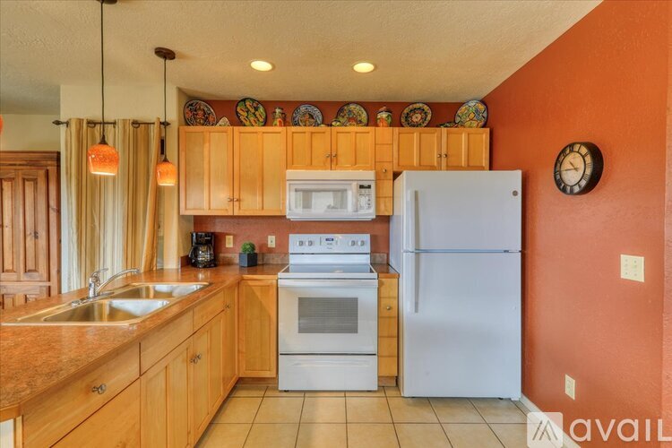 A kitchen with a white oven and refrigerator, wooden cabinets, and a clock on the wall.