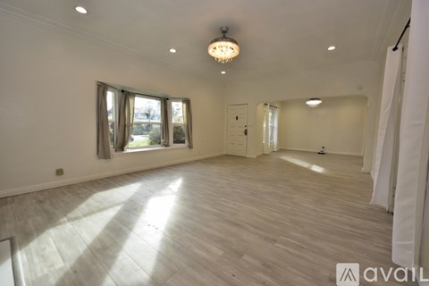A spacious room with wooden flooring and a chandelier hanging from the ceiling.