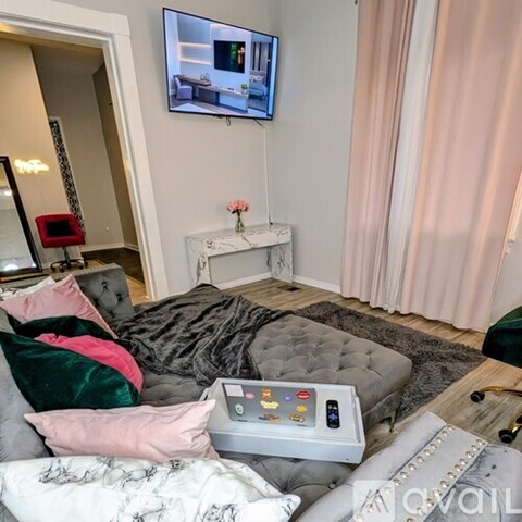 A living room with a grey tufted ottoman and a television mounted on the wall.