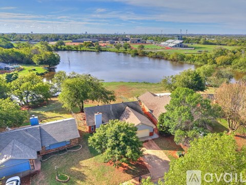 A house with a blue roof is surrounded by trees and a body of water.