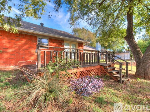A red brick house with a porch and a tree in front.