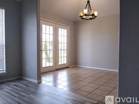 A room with a chandelier, tiled floor, and a large window with a view of trees.