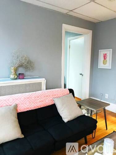 A black couch with a pink pillow and a small table in front of it.