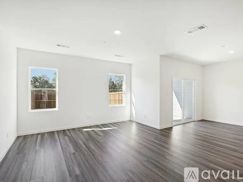 A spacious room with wood flooring and two windows.